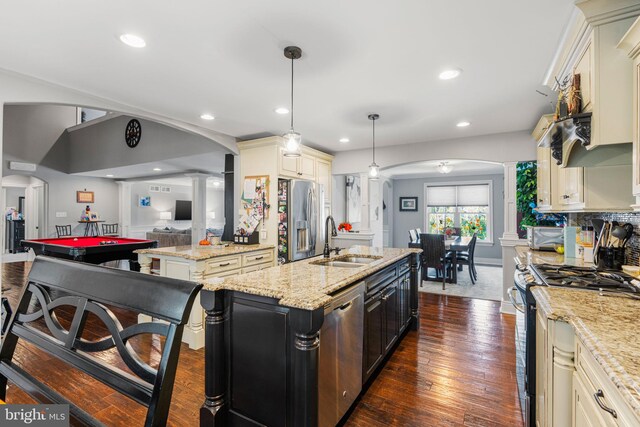 kitchen featuring appliances with stainless steel finishes, sink, decorative light fixtures, light stone counters, and a kitchen island with sink