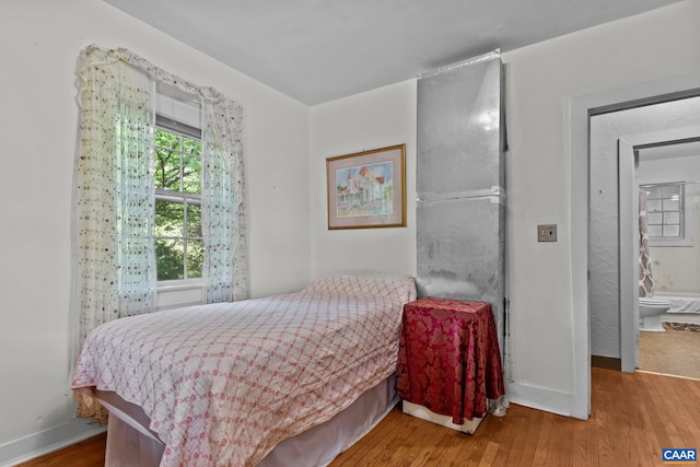 bedroom with ensuite bath and wood-type flooring