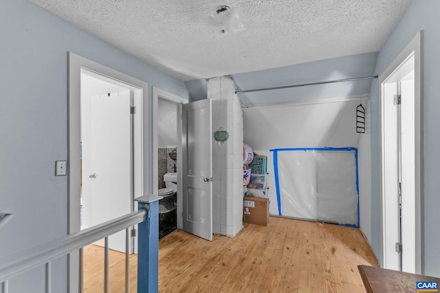 bedroom with connected bathroom, a textured ceiling, and light wood-type flooring