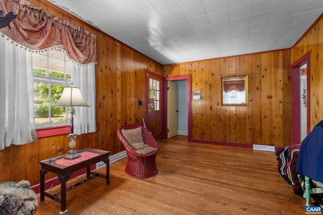 living area with crown molding, wood walls, and hardwood / wood-style floors