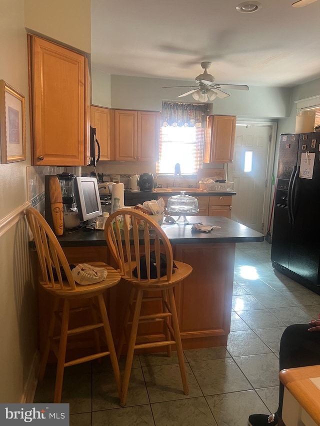 kitchen with tile patterned floors, a kitchen breakfast bar, black refrigerator with ice dispenser, and ceiling fan