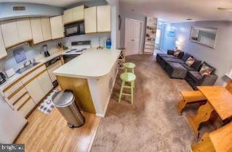 kitchen with light countertops, electric range, cream cabinets, black microwave, and a kitchen bar