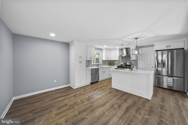 kitchen with appliances with stainless steel finishes, wall chimney range hood, decorative light fixtures, and white cabinetry