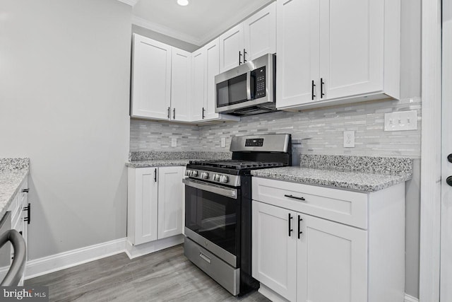 kitchen with white cabinets, appliances with stainless steel finishes, ornamental molding, light hardwood / wood-style floors, and light stone counters