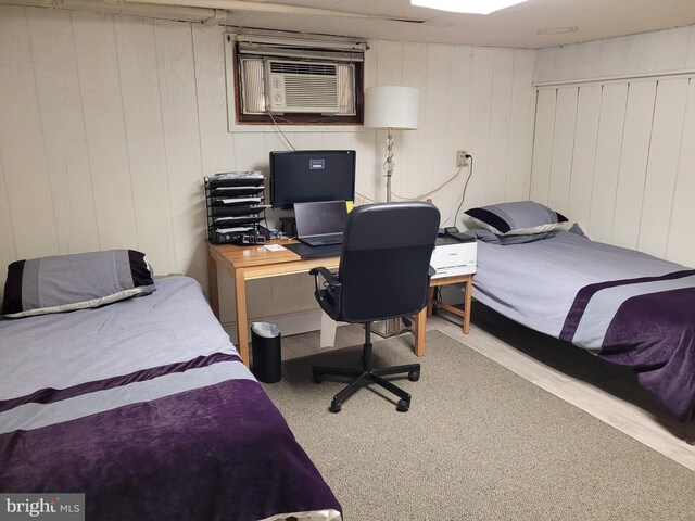 bedroom with an AC wall unit, wooden walls, and light colored carpet