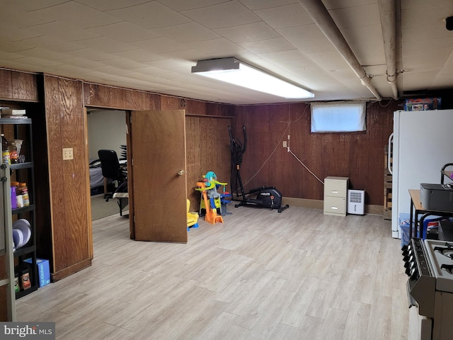 basement featuring white fridge, light hardwood / wood-style floors, and wooden walls