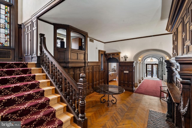 stairs with a high ceiling, parquet floors, and crown molding