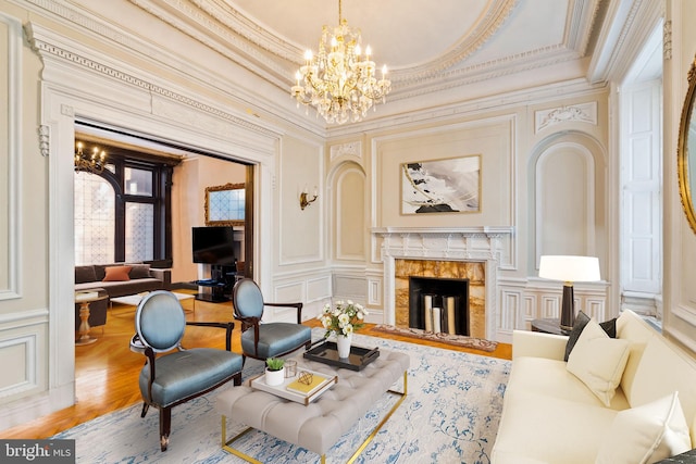 living area featuring wood-type flooring, crown molding, a raised ceiling, a premium fireplace, and a chandelier