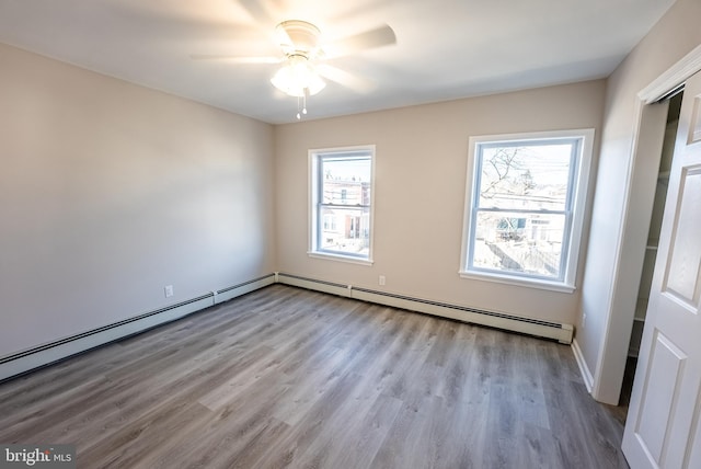 spare room featuring ceiling fan, baseboard heating, and light wood-type flooring