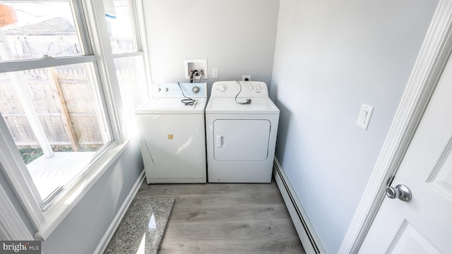 clothes washing area featuring light hardwood / wood-style flooring, baseboard heating, and washer and clothes dryer