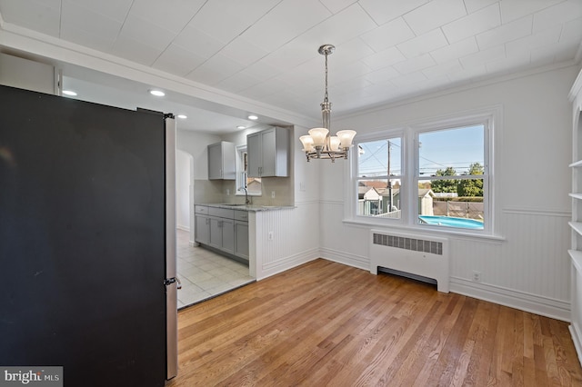 unfurnished dining area featuring radiator, sink, crown molding, a notable chandelier, and light wood-type flooring