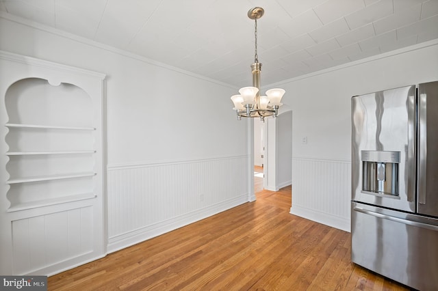 unfurnished dining area featuring crown molding, a notable chandelier, built in features, and hardwood / wood-style floors