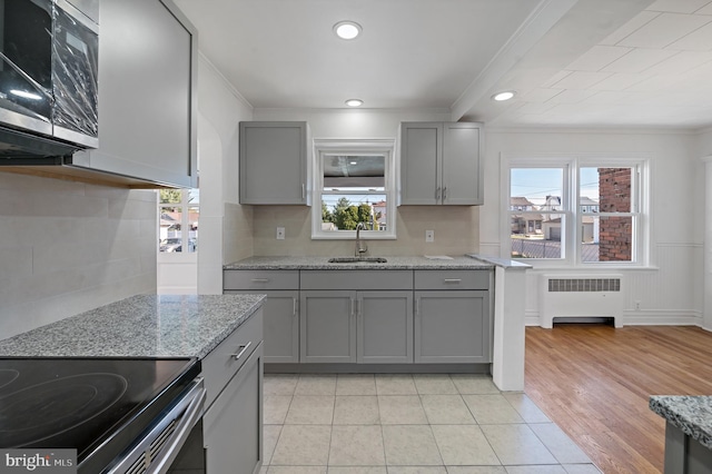 kitchen featuring radiator, light hardwood / wood-style floors, sink, and light stone counters