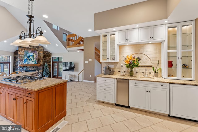 kitchen featuring lofted ceiling, a stone fireplace, pendant lighting, white cabinetry, and appliances with stainless steel finishes