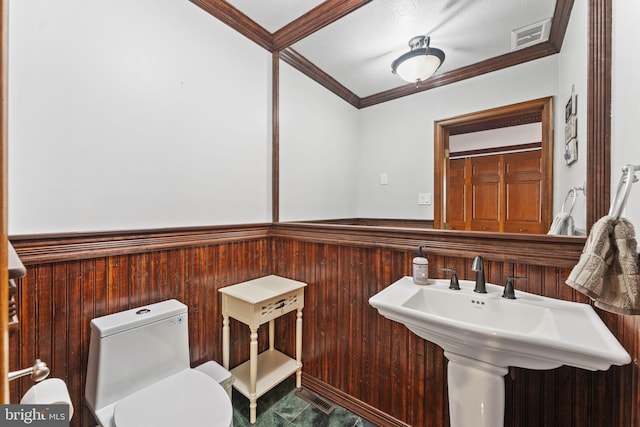 bathroom featuring sink, a textured ceiling, toilet, wooden walls, and crown molding