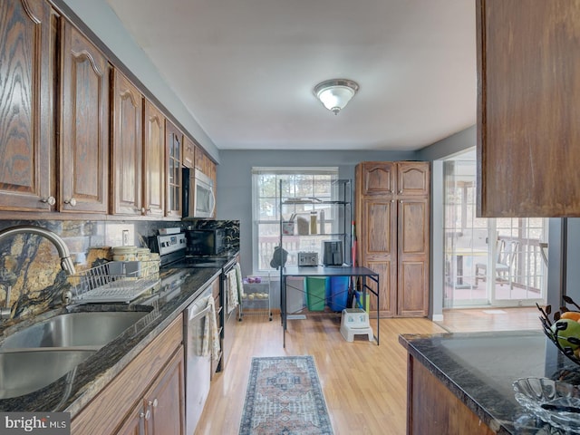 kitchen featuring dark stone counters, stainless steel appliances, a sink, and light wood-style floors