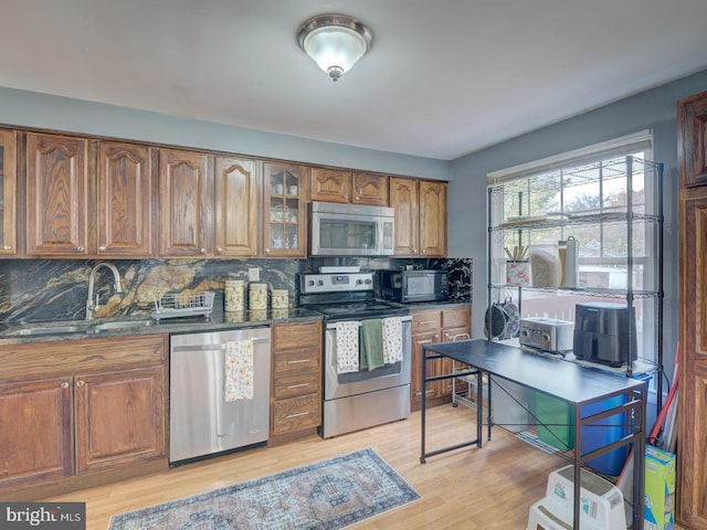 kitchen with brown cabinetry, glass insert cabinets, tasteful backsplash, a sink, and appliances with stainless steel finishes