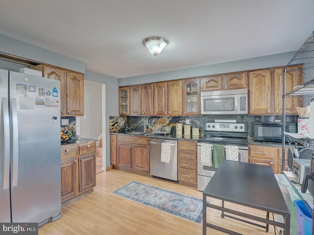 kitchen with brown cabinetry, light wood-type flooring, tasteful backsplash, and stainless steel appliances