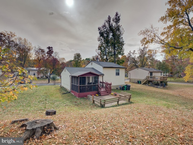 back of house featuring a lawn, a wooden deck, and a sunroom