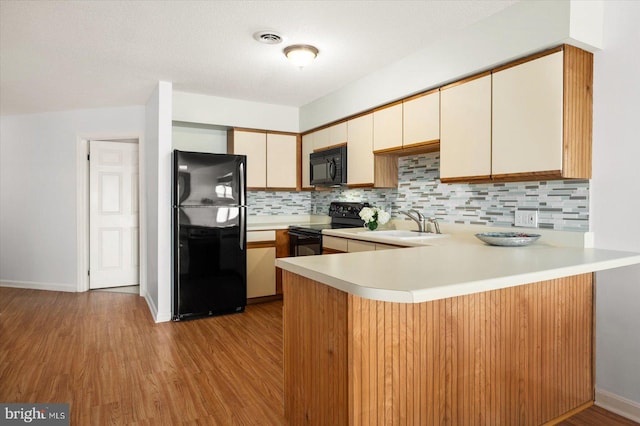 kitchen featuring black appliances, kitchen peninsula, light hardwood / wood-style floors, and tasteful backsplash