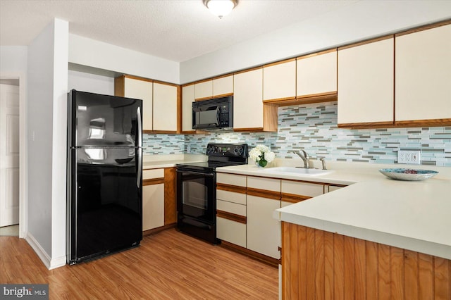 kitchen featuring decorative backsplash, a textured ceiling, light hardwood / wood-style flooring, black appliances, and sink