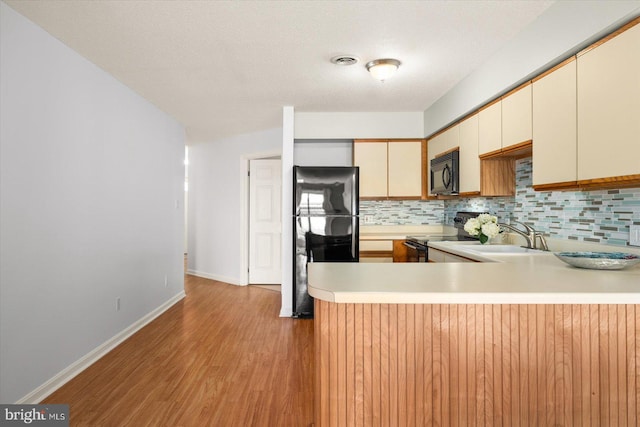 kitchen with black appliances, sink, cream cabinetry, kitchen peninsula, and light hardwood / wood-style flooring