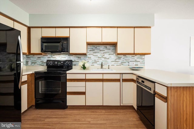 kitchen featuring tasteful backsplash, black appliances, sink, light wood-type flooring, and kitchen peninsula