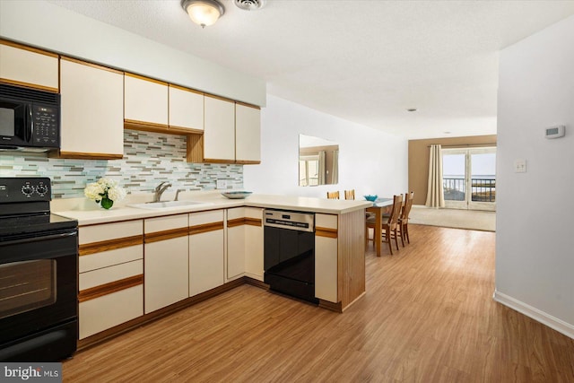 kitchen featuring black appliances, sink, kitchen peninsula, decorative backsplash, and light hardwood / wood-style flooring