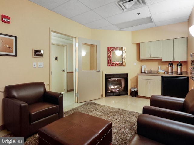 living room featuring sink, light tile patterned flooring, a fireplace, and a paneled ceiling