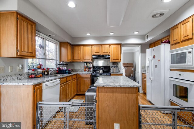 kitchen with a center island, sink, light stone countertops, light wood-type flooring, and white appliances