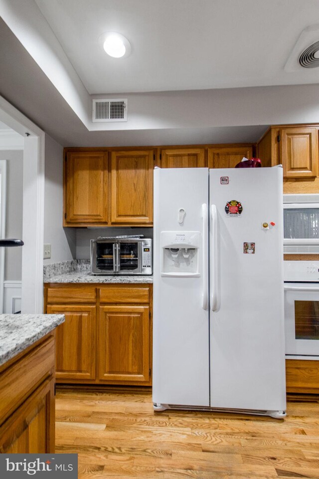 kitchen with light wood-type flooring, white appliances, and light stone countertops