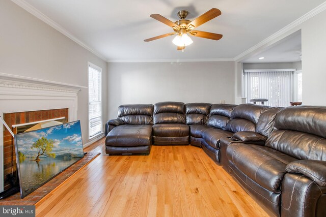 living room featuring ceiling fan, wood-type flooring, a brick fireplace, and ornamental molding