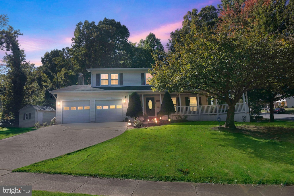 view of front of house with covered porch, a yard, and a garage