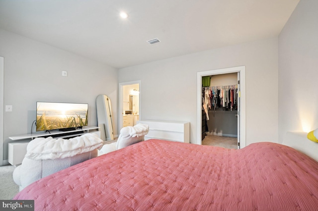 bedroom with connected bathroom, light colored carpet, a walk in closet, and a closet