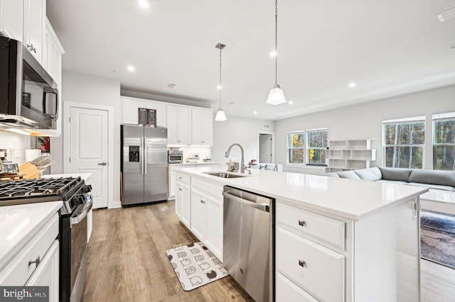 kitchen with stainless steel appliances, white cabinetry, sink, an island with sink, and light hardwood / wood-style flooring