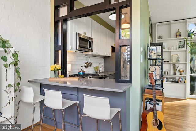 kitchen with kitchen peninsula, backsplash, a breakfast bar area, light hardwood / wood-style floors, and stainless steel appliances