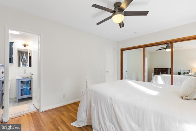 bedroom with ceiling fan, ensuite bathroom, light hardwood / wood-style floors, a closet, and sink