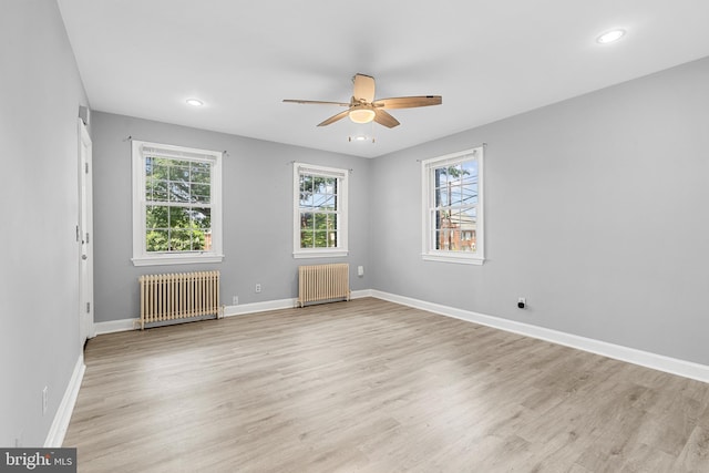 spare room with ceiling fan, light wood-type flooring, and radiator