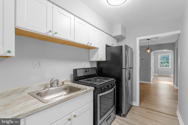 kitchen featuring appliances with stainless steel finishes, sink, light wood-type flooring, white cabinetry, and radiator