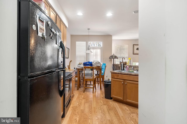 kitchen with sink, pendant lighting, black appliances, and light hardwood / wood-style floors