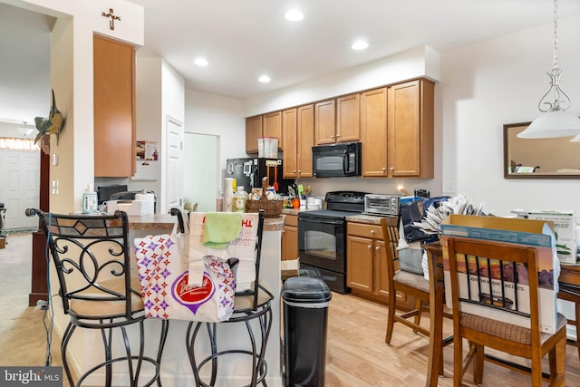 kitchen with hanging light fixtures, kitchen peninsula, a breakfast bar area, black appliances, and light wood-type flooring