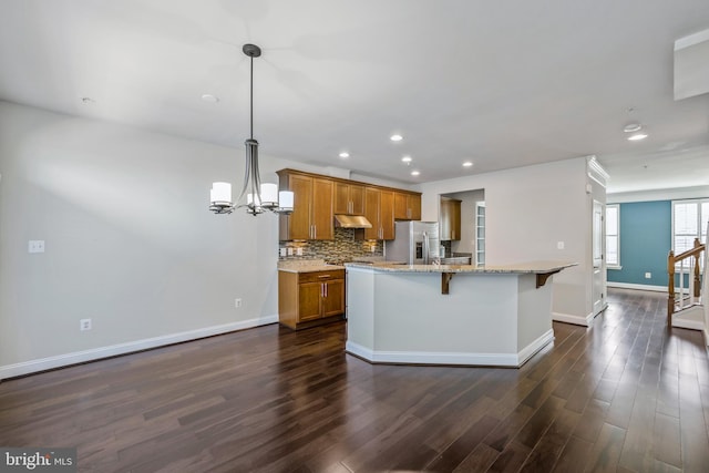 kitchen featuring stainless steel fridge with ice dispenser, a kitchen bar, dark hardwood / wood-style floors, decorative light fixtures, and light stone counters