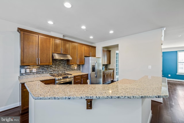 kitchen featuring light stone countertops, stainless steel appliances, a kitchen bar, and dark hardwood / wood-style flooring