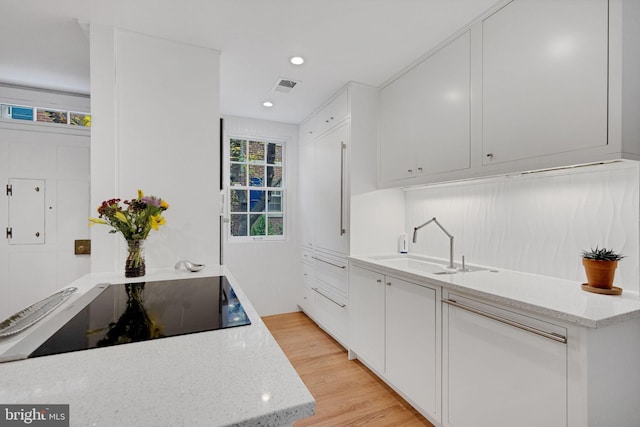 kitchen with light stone countertops, black electric stovetop, sink, light hardwood / wood-style flooring, and white cabinets