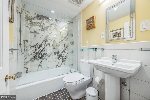 bathroom featuring tile patterned flooring, toilet, combined bath / shower with glass door, and tile walls