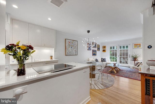 kitchen with pendant lighting, white cabinets, light hardwood / wood-style flooring, light stone countertops, and ornamental molding