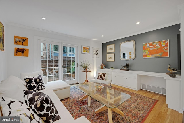 living room with crown molding, built in desk, and light wood-type flooring