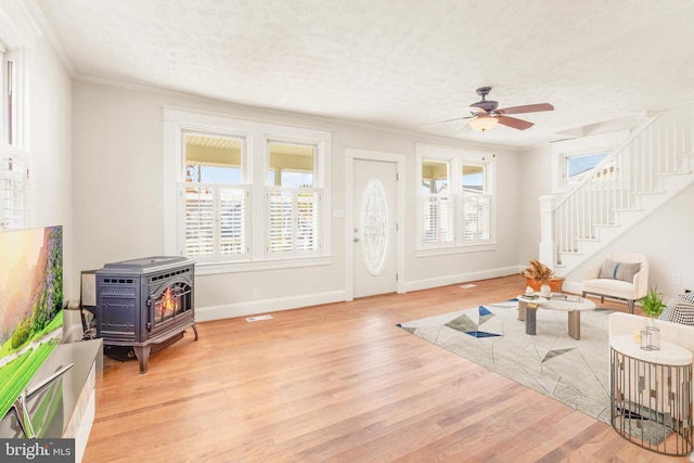 living room featuring a textured ceiling, a wood stove, ceiling fan, ornamental molding, and light hardwood / wood-style flooring