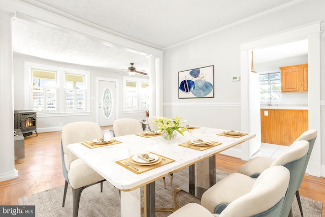 dining space with crown molding, ceiling fan, light wood-type flooring, and a wood stove