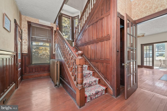 stairs featuring french doors, radiator, hardwood / wood-style floors, and a textured ceiling